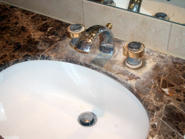 Limescale damage on a marble vanity top caused by leaking taps