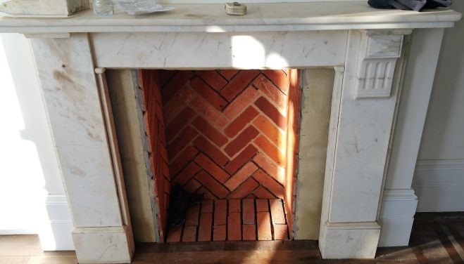 A STAINED AND DAMAGED CARERRA MMARBLE FIREPLACE