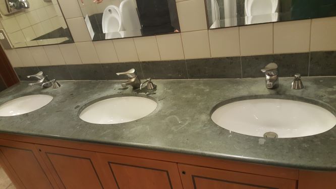 A green Jura limestone vanity top with limescale damage around the taps and numerous etch marks caused strong cleaning products
