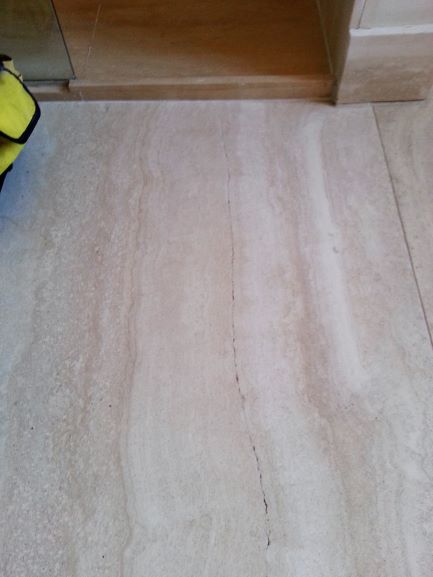 A cracked Travertine floor  tile in a bathroom, cleaned before a repair