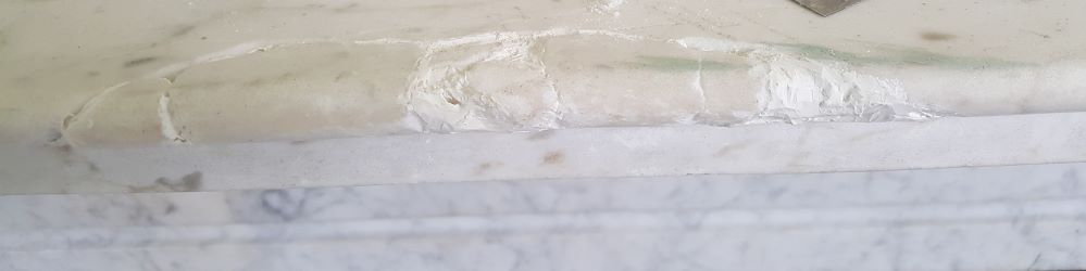 Repairing a chip on a marble shelf, filling the large gaps with a white resin filler.